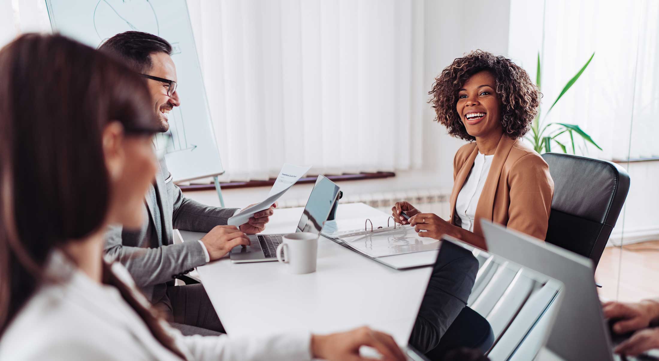 Hero-Image-web Business Woman sits at a table with colleagues.