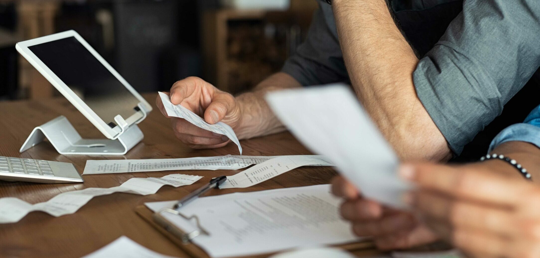 Mature smalll business owners calculating finance bills of their activity. Business people using calculator to work. Closeup hands of man and woman calculating bills and expenses.