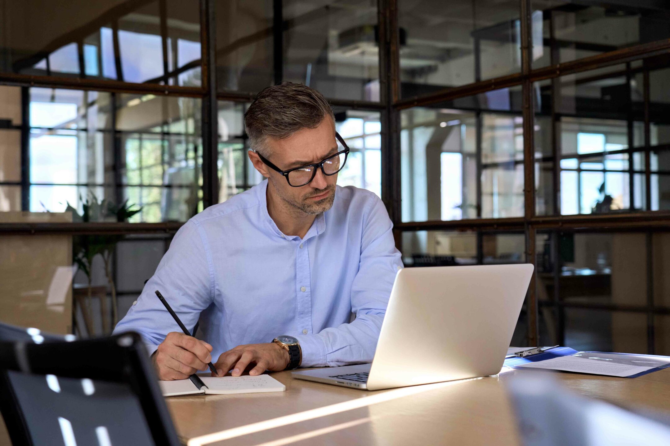 Mature business man executive manager looking at laptop computer watching online webinar training or having virtual meeting video conference taking notes, doing market research working in office.