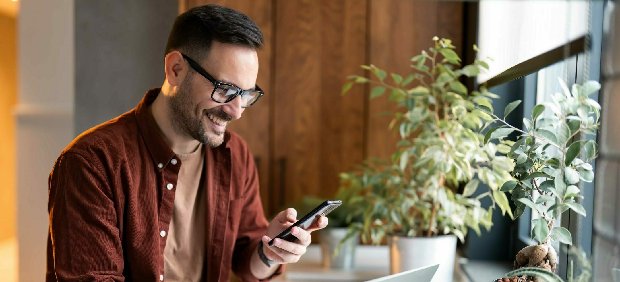 Satisfied,Modern,Millennial,Man,In,Stylish,Casual,Clothes,Using,Smartphone Satisfied modern millennial man in stylish casual clothes using smartphone and laptop computer for electronic banking, making reservation, online shopping and payments while spending time at home.