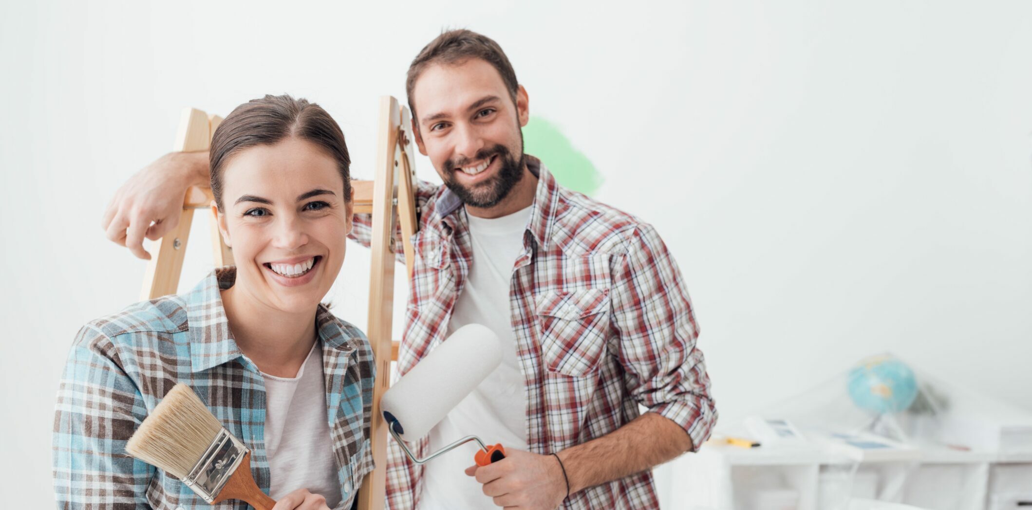Creative young couple renovating their house and painting walls, they are posing together and smiling at camera